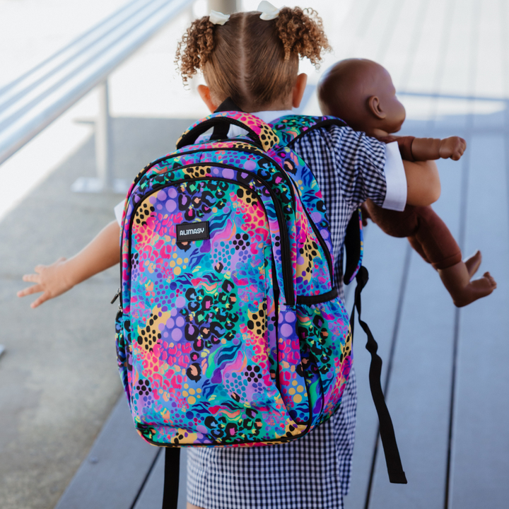 Child with a colorful kids backpack holding a doll standing outside school