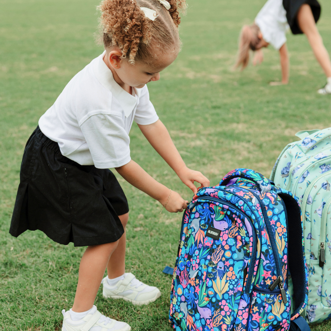 Child interacting with a colourful blue sealife design backpack on grass