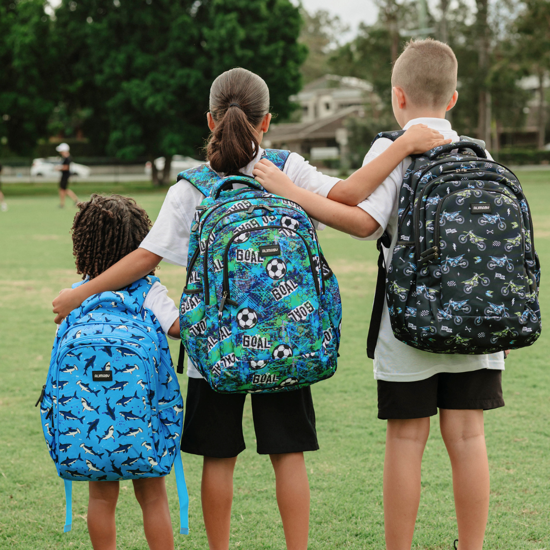 Three children wearing patterned backpacks on a grassy field